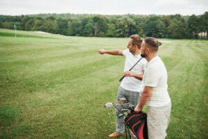 Two stylish men holding bags with clubs and walking on golf course